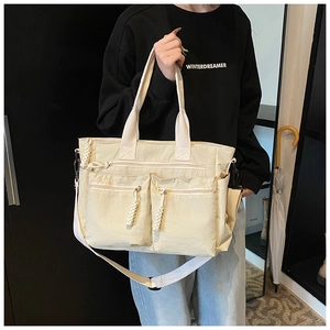 Detail view of cream canvas tote bag featuring double front zip pockets and woven pullers