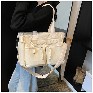 Detail of off-white multi-pocket tote bag with woven rope zippers and adjustable strap