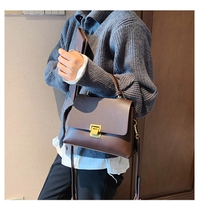 Détail d'un sac bandoulière marron foncé avec boucle dorée porté sur un pull gris chic