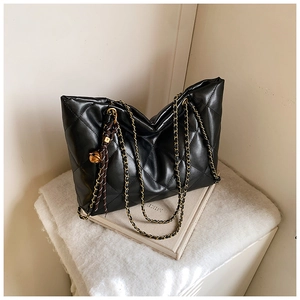 Detail of black quilted tote bag with gold chain strap and decorative sphere pendant