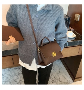 Détail d'un sac à main en cuir mat marron foncé avec fermoir doré dans un café