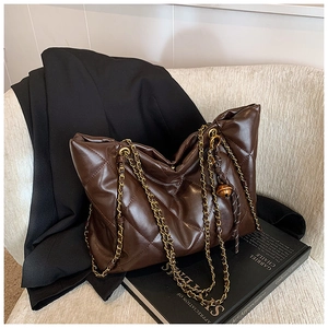 Detail of dark brown quilted tote bag with gold chain strap on a black blazer
