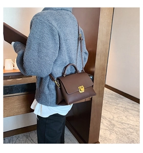 Vue détaillée du sac à main en cuir marron foncé avec fermoir doré sur un modèle femme