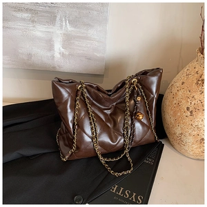 Close-up of brown quilted tote bag with gold chain strap and spherical charm on a blazer