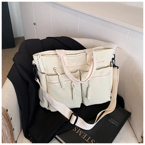 Detail of off-white multi-pocket tote bag featuring woven zippers and adjustable strap