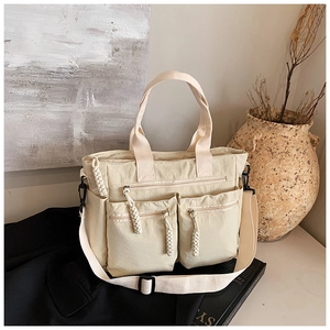 Detail view of beige nylon tote bag with three front zip pockets and woven rope pullers