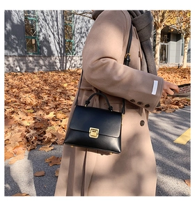 Gros plan d'un sac à main chic en cuir noir avec fermoir doré sur fond de manteau beige