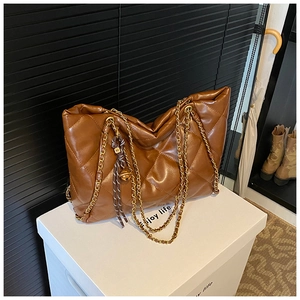 Detailed view of brown quilted tote bag with gold chain straps and M letter charm detail