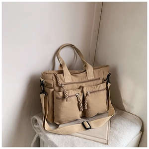Detail of khaki tote bag featuring multiple zipper pockets and woven rope zipper pulls