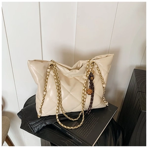Detail of quilted leather tote bag with gold chain strap and decorative woven knot charm