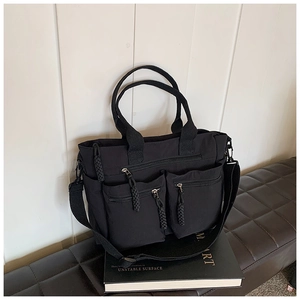 Close-up of black nylon tote bag featuring front dual zipper pockets and a wide strap