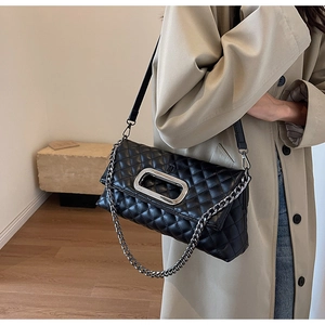 Nahaufnahme der schwarzen Stepptasche mit Silberschnalle und Kette auf beigem Trenchcoat