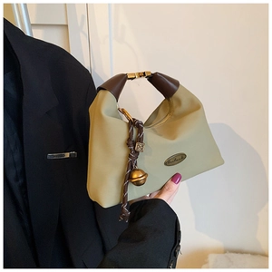 Detalle del bolso hobo de lona caqui con asa de cuero marrón y etiqueta metálica artesanal