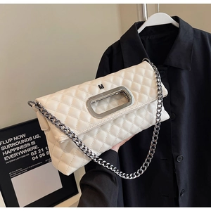 Detailansicht der cremefarbenen Stepptasche mit Metallic-M-Logo und silberner Kette