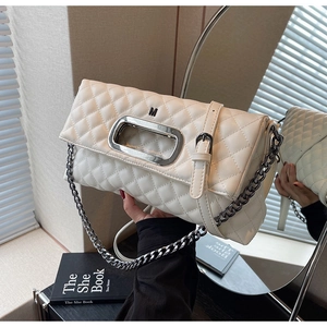 Detail der cremefarbenen Stepptasche mit ovalem Metallgriff und Kettenriemen