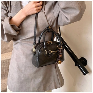 Detail of a vintage black matte leather handbag featuring gold horsebit and woven charm