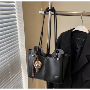 Detail of minimalist black tote bag with silver sphere hardware and plush charm pendant