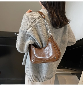 Détail d'un sac sous le bras marron foncé brillant avec chaîne portée sur un pull gris