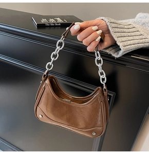Détail d'un sac à bandoulière en cuir marron brillant avec une grosse chaîne argentée