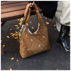 Detailed view of brown quilted tote bag featuring small white bear embroidery patterns