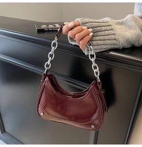 Détail du sac demi-lune bordeaux verni avec une grosse chaîne argentée et des rivets