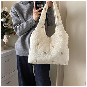 Close-up of white quilted tote bag featuring brown bear embroidery and metal snap closure