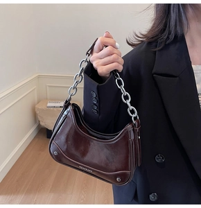 Détail du sac sous le bras en cuir verni marron foncé avec une grosse chaîne argentée