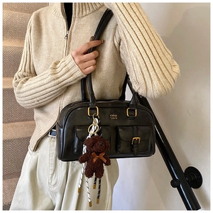 Detailansicht der schwarzen Schultertasche aus Kunstleder mit Goldschnallen und Bär-Anhänger