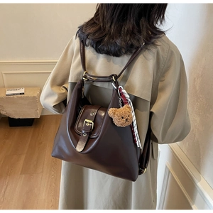 Detail of dark brown leather tote bag with metal buckle, scarf, and cute plush bear charm