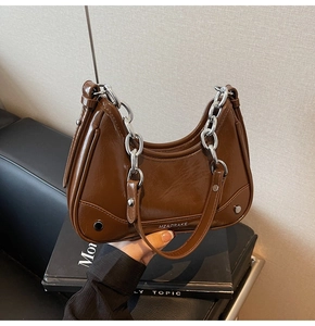 Détail d'un sac croissant marron brillant avec chaîne argentée et accents de rivets