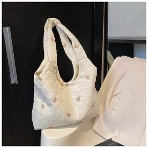 Detailed view of white quilted tote bag with pink bear embroidery on a white chair