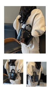 Detail of black glossy leather bucket bag with gold hardware and pretzel charm