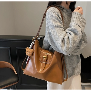 Detail view of brown matte leather tote bag with golden buckle and plush bear pendant