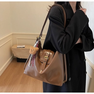 Brown leather shoulder bag with vintage metal buckle and plush bear charm on a model