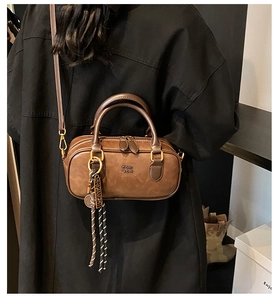 Detail view of a vintage brown leather Boston bag with metal pendant and logo embossing