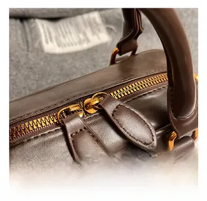 Close-up of matte dark brown leather Boston bag featuring premium gold hardware zippers