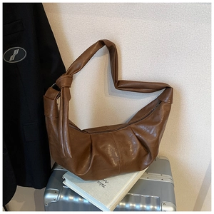 Close-up of brown PU leather crescent bag with knot detail and smooth zipper on a suitcase