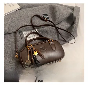 Detail of dark brown Boston bag with smooth leather texture and tennis racket charm