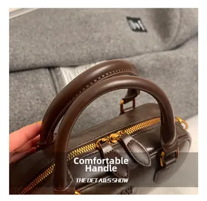 Close-up of brown leather Boston bag with dual gold zippers and stitching details