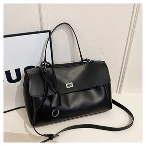 Detail of black textured leather handbag featuring a metal twist lock and structured top handle