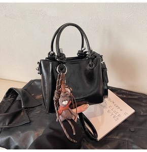 Détail d'un sac cabas en cuir noir brillant avec un ourson marron et une sangle tressée