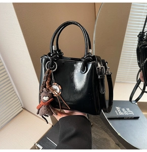 Détail du sac à main en cuir ciré noir avec charm ours et finitions dorées élégantes