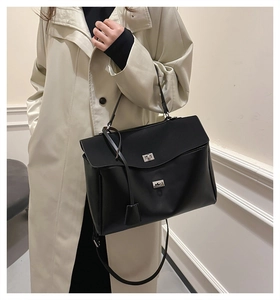 Detail of a black leather handbag with silver metal buckles on a light trench coat