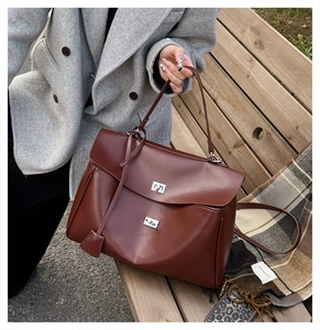 Close-up of a burgundy leather handbag with silver lock on a wooden bench outdoors