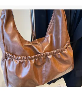 Detailansicht der braunen PU-Lederstruktur und des gefalteten Taschendesigns vorne