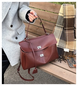 Detail of burgundy lychee leather handbag with silver lock and pendant on wood bench