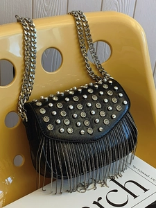 Chic black crossbody bag with silver studs and long fringe on a yellow chair