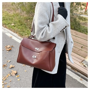 Close-up of a burgundy leather satchel with silver clasp worn with a grey wool coat