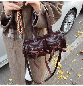 Gros plan d'un sac cylindrique en cuir verni marron foncé avec nœuds décoratifs