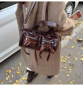 Détail du sac bandoulière en cuir verni marron foncé avec nœuds décoratifs et poches avant